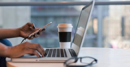 Frau arbeitet remote mit Smartphone und Laptop